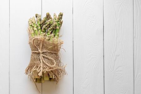 Asparagus shoots are tied with a jute rope on white boards. Fresh asparagus is wrapped with a jute cloth on a white wooden background with a copy of space.の写真素材