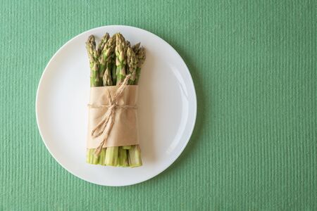 Asparagus shoots are tied with a jute rope on a white plate. Fresh asparagus on a green background.の写真素材