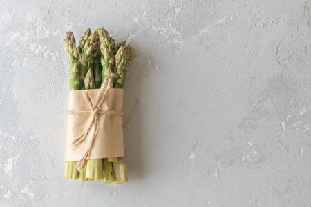 Asparagus shoots are tied with a jute rope on a grey concrete background. Fresh asparagus is wrapped in paper on a concrete background with a copy of space.の写真素材