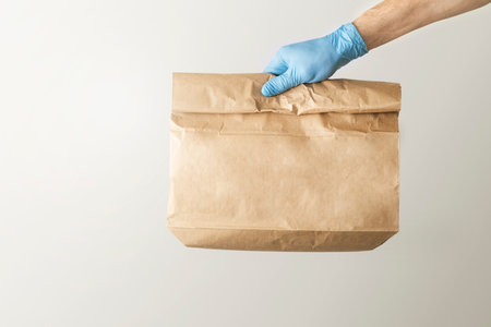 The concept of food delivery. A man's hand in medical gloves holds a paper bag.