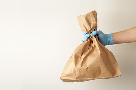 The concept of food delivery. A man's hand in medical gloves holds a paper bag.