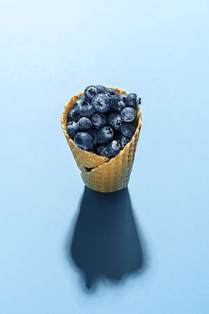 Frozen blueberries in waffle horn on a blue background. Conceptual minimalism.の写真素材