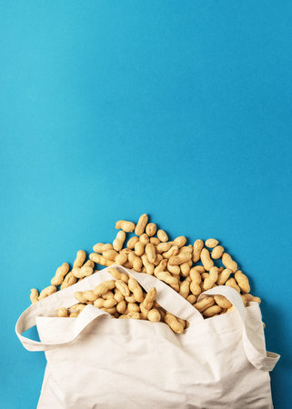 Dried raw peanuts from a fabric bag on a blue background with a copy of the space.
