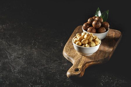 Purified macadamia nut in a white bowl on a dark background with a copy of space.