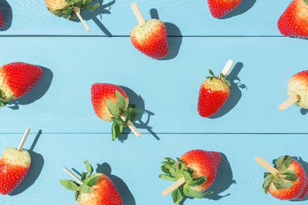 Juicy strawberries on a stick on a blue background with sharp shadows.の写真素材