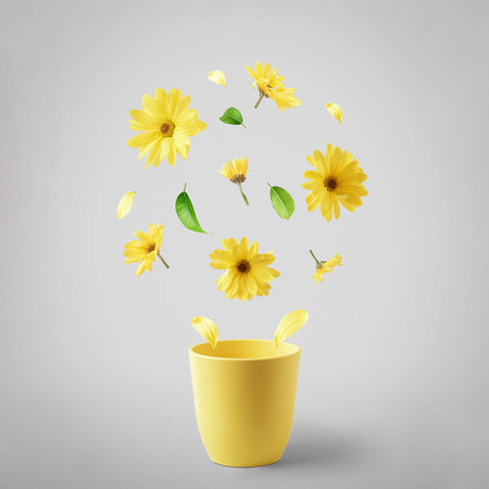 Yellow cup with flying yellow flowers on a gray background. The concept of spring.