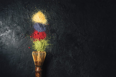 Various matcha tea powders with a whisk on a dark concrete background with a copy of space.