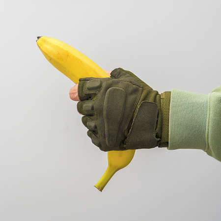 A man's military hand holds a banana on a gray background.の写真素材