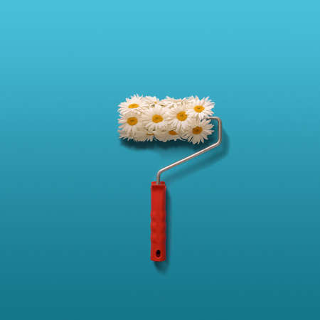 Creative composition of camomiles and paint roller on blue background.の写真素材