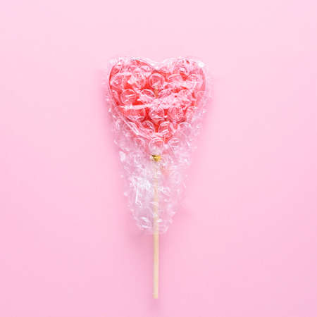 Creative mental health concept. Single heart-shaped lollipop wrapped in bubblegum on a pink background.の写真素材