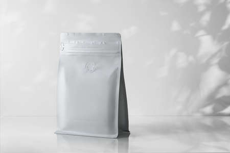 Mock-up of a coffee package on a gray background with stiff shadows from the leaves.の写真素材