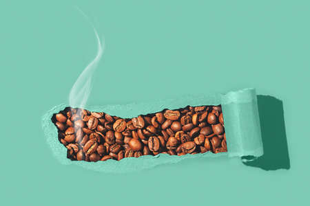 Creative coffee flat lay. Aromatic coffee beans through torn green paper.の写真素材