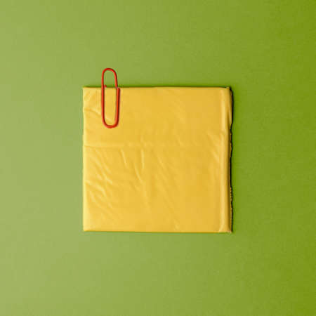 Creative layout of food on a green background. A square slice of cheese under a paper clip. health diary.の写真素材