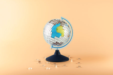 Creative collage of a globe and a scattering disco ball on an orange background.の写真素材
