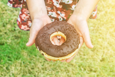 Girl holding a chocolate donut standing on the lawn.の写真素材