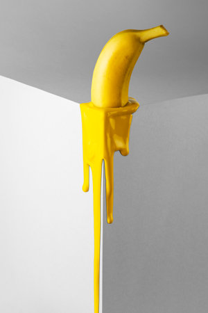 Yellow banana melts on the corner of the gray cube. Minimalist fruit concept.の写真素材