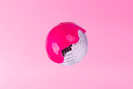 Mirror ball doused with pink paint on a pink background. creative music concept.の写真素材
