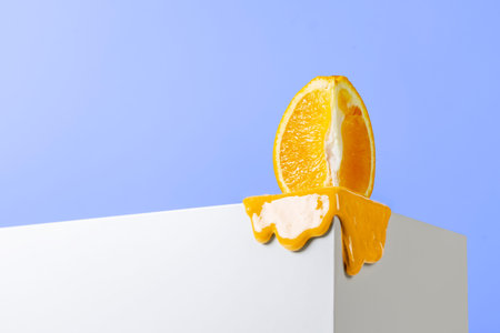 Melting orange piece standing at the end of the corner of the white block opposite the blue background.の写真素材
