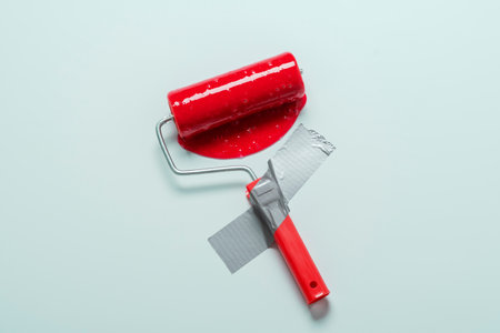 Paint roller affixed with gray duct tape to blue wall with spreading red paint. Creative renovation concept.の写真素材
