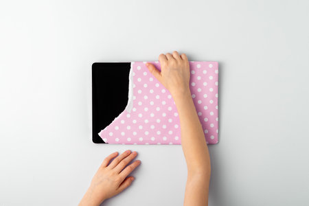Child's hands take a gifted tablet wrapped in pink gift paper on a blue background. Top view.の写真素材