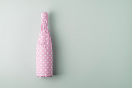 Champagne bottle packaged in pink polka dot gift paper on blue pastel background with copy space. Creative gift and holiday concept.の写真素材