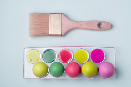 Multicolored Easter eggs in egg tray with multicolored pastel paints with brush on blue background.の写真素材