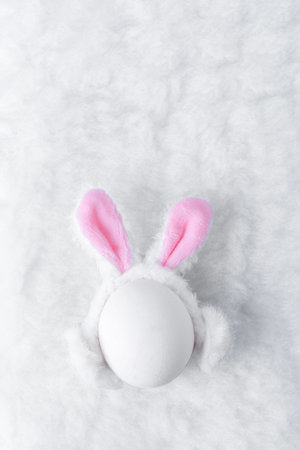 Creative Easter concept. White egg with fluffy ears of Easter bunny on fluffy soft white background with copy space.の写真素材