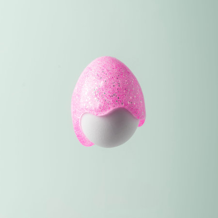 Easter egg painted in pink paint with glitter on a blue pastel background. Creative Easter concept.の写真素材