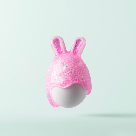 Easter egg with bunny ears painted with pink paint with glitter on blue pastel background. Creative Easter concept.の写真素材