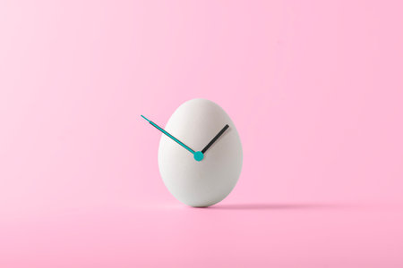 Creative Easter concept. White Easter egg with hour hands on pink background. Easter time.の写真素材