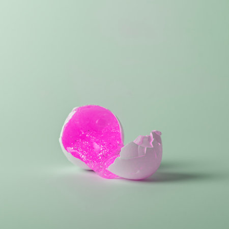 Broken white Easter egg with pink spreading liquid on blue pastel background. Easter concept.の写真素材