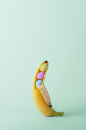 Creative Easter concept. Opened banana with colorful Easter eggs on green pastel background with copy space.の写真素材