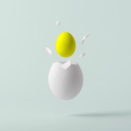 Creative Easter concept. Yolk flies out of a broken white egg in the shape of a yellow Easter egg on a blue pastel background.の写真素材