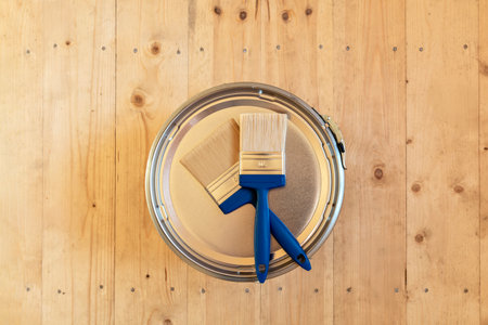 Two blue-handled paintbrushes on the lid of a paint can on a wooden floor, emphasizing wood surface protection in a wooden houseの写真素材
