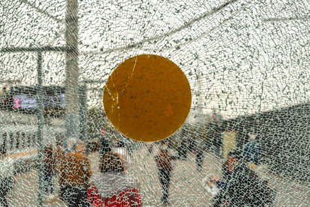 Shattered glass with yellow marker against urban background, blurred figures and architecture create dynamic atmosphereの写真素材