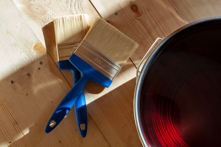 Two blue-handled paintbrushes on a light wooden floor next to a varnish can, illustrating wood floor treatment in a houseの写真素材