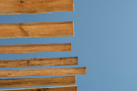 View from below of wooden roof sheathing beams of a frame house against clear sky