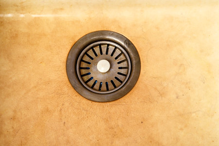 Dirty kitchen sink with metal drain in center, covered with yellow plaque and traces of contamination. Worn surface with visible cracks and stains.の写真素材