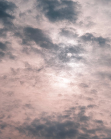 Dramatic clouds in soft pastel shades of pink and gray partially cover the sun, creating a moody sky background. Atmospheric and minimalistic.の写真素材