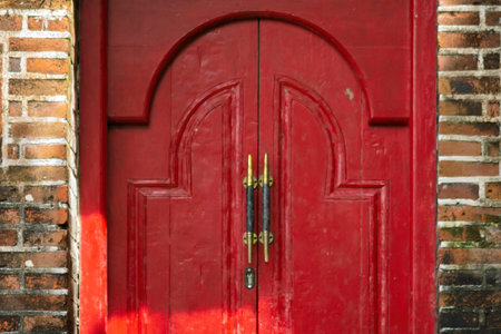 An old red wooden door with curved patterns set in a brick wall. Decorative elements and patina highlight its historical character.の写真素材