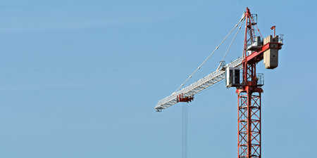 Red tower crane rises against clear blue sky, leaving wide negative space ideal for banner text, concept of construction and development.の写真素材