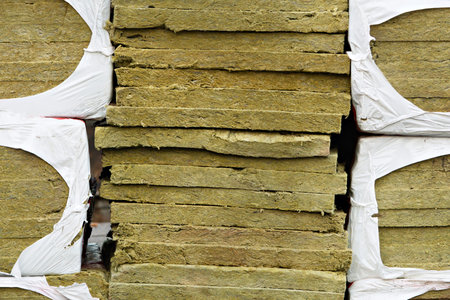 Stack of mineral wool insulation boards in torn plastic wrap shows textured surface of construction...