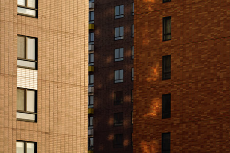 Warm-toned building facades with repetitive windows and soft shadows create a calm urban background with structured vertical geometry.の写真素材