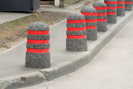 Concrete bollards with bright red stripes line urban sidewalk, creating visual rhythm and enhancing pedestrian safety in cityscape.の写真素材