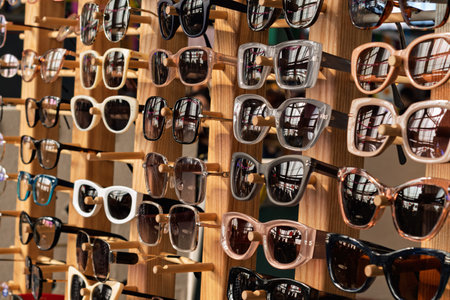 Various stylish sunglasses with different frames are displayed on a wooden rack, reflecting light and creating a vibrant summer mood.の写真素材