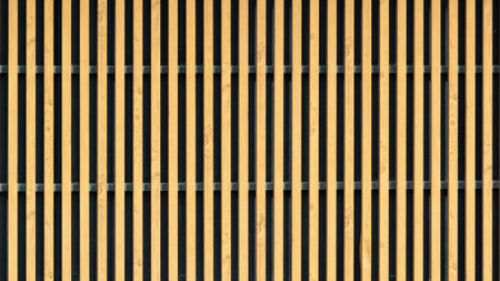 Vertical wooden slats arranged in a regular pattern create a modern decorative screen, combining natural texture with geometric symmetry.の写真素材