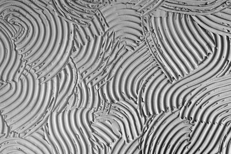 Abstract close-up of artistic gray plaster with swirling relief patterns, emphasizing dynamic movement, texture and tactile visual interest for creative backgrounds.の写真素材