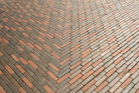 Symmetrical herringbone pattern of red and gray bricks creates dynamic geometric design on a clean...