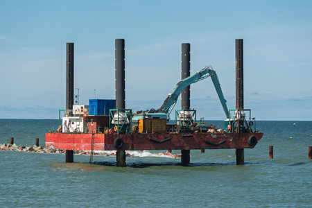 Marine platform with excavator stands on steel supports in the sea, used for coastal construction and underwater engineering projects.の写真素材