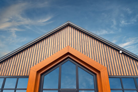 Modern wooden building facade with triangular roof and large glass windows stands out against dramatic evening sky, symbolizing urban style.の写真素材